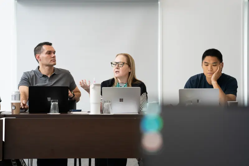 Three colleagues at a workshop table, one mid-point with laptops open in front of them.