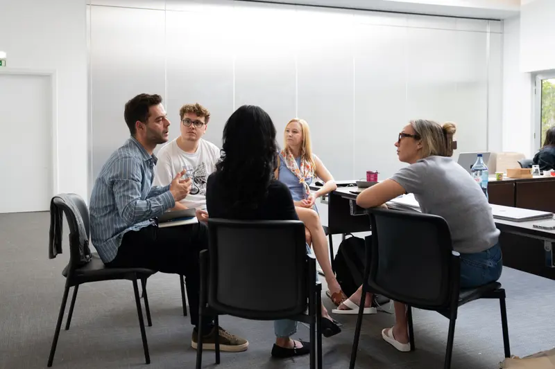 Five colleagues pulled into a circle of chairs for a discussion away from the tables.