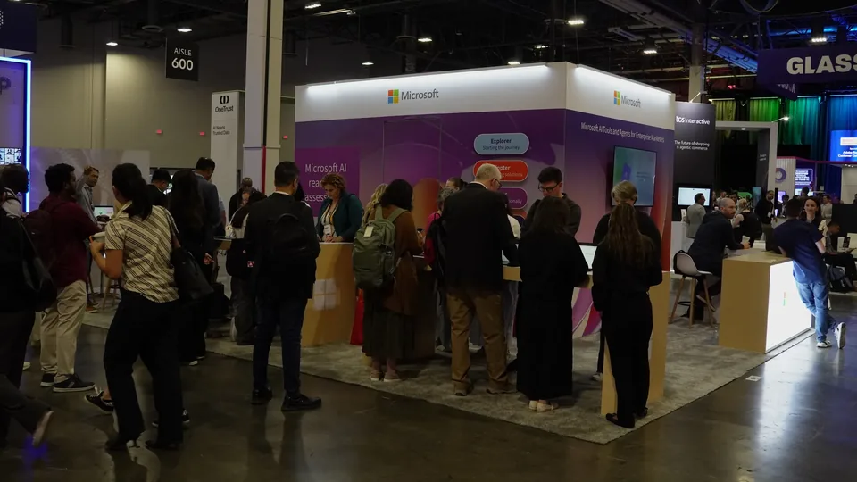 The stand seen from the aisle, attendees gathered around its demo counters under a lit ceiling fascia.