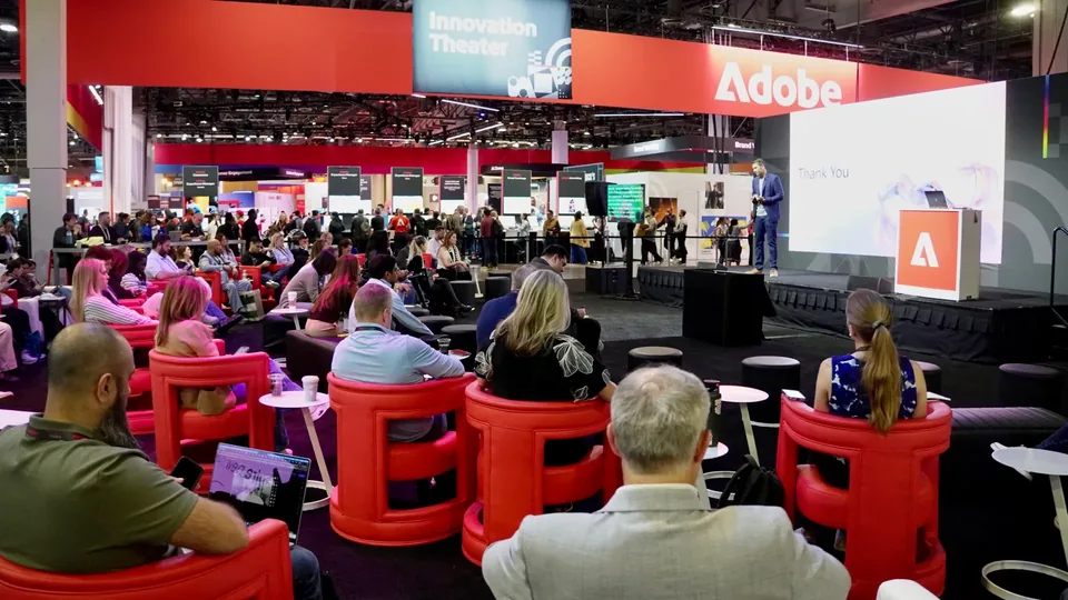 The Adobe Innovation Theater, an audience in red lounge chairs facing a lit stage.