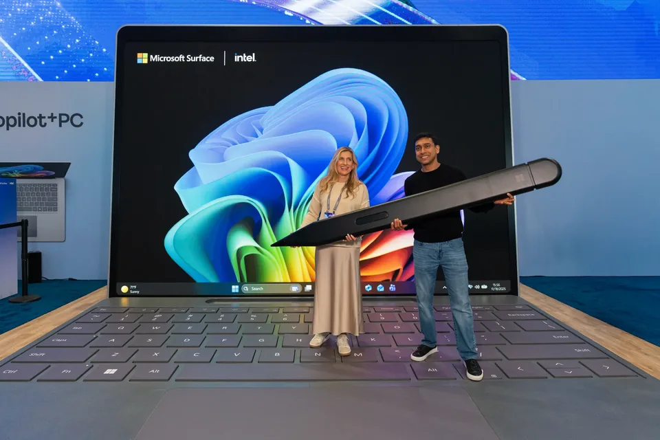 Two people holding an oversized Surface pen in front of a giant Surface laptop set piece.