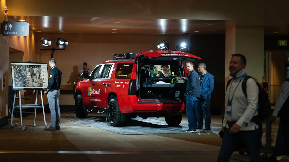 A red Microsoft-branded pickup truck lit inside the venue, attendees at a display board beside it.