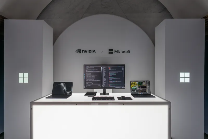 A vaulted briefing room with an NVIDIA and Microsoft lockup on the back wall, a dual-monitor developer workstation on a softly lit white plinth.