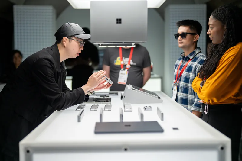 A visitor lifts a device from the display table as three others look on, a laptop suspended overhead.
