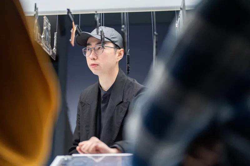 A visitor in a cap studies a device at the plinth, framed between two out-of-focus figures.