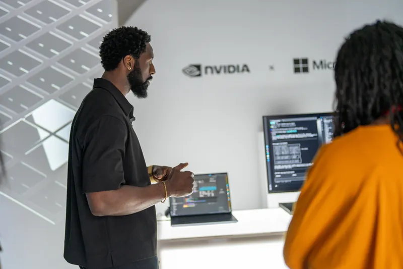 A presenter gestures toward a screen of code beneath the NVIDIA and Microsoft lockup while an attendee listens.
