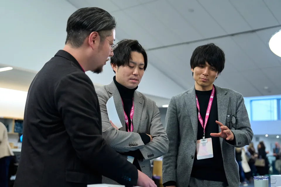 Three attendees examining a device together in a bright hall.