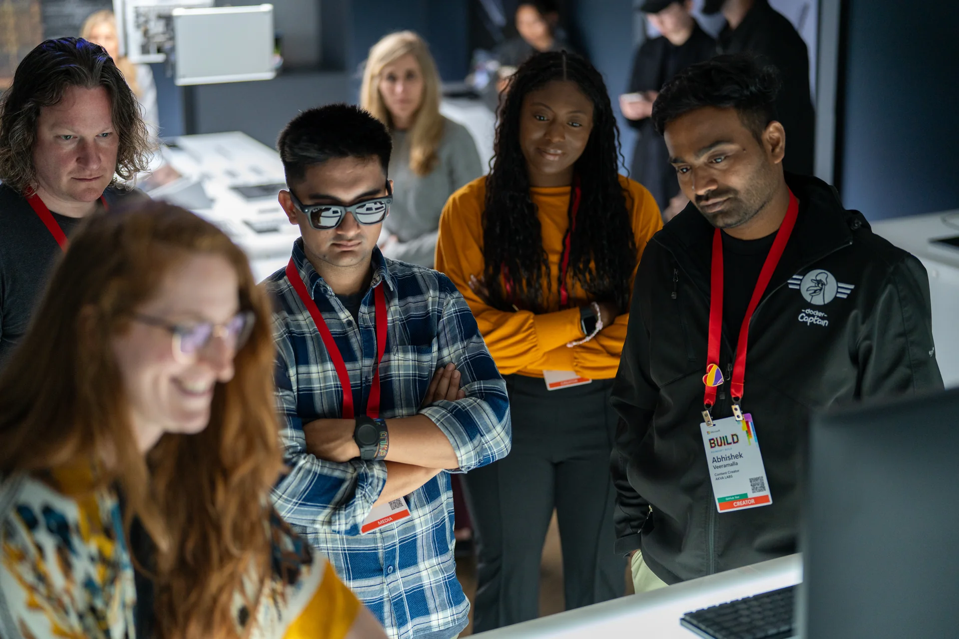 Attendees clustered around a workstation at a hands-on session, lanyards and screens catching the light.