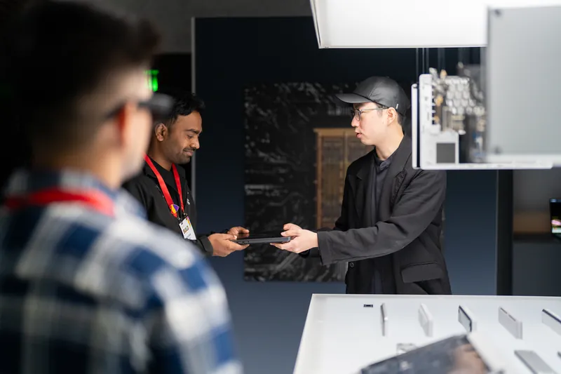 Two attendees examining hardware at a lit plinth in the darkened gallery.