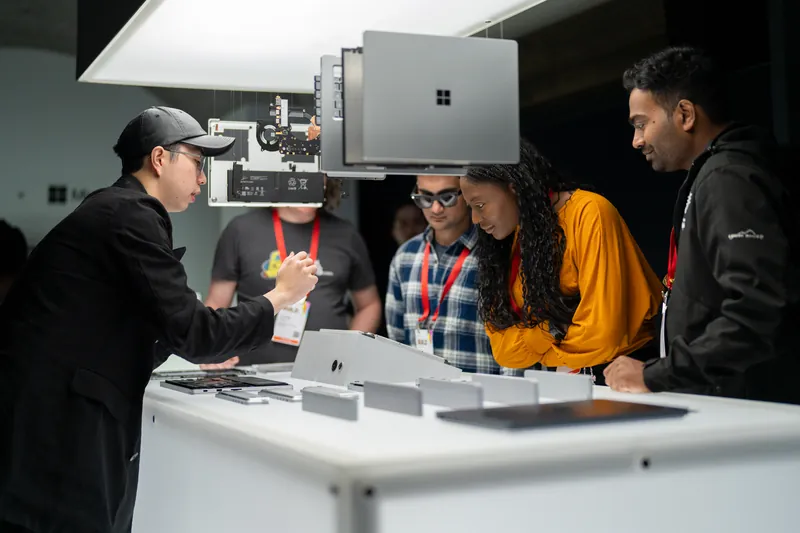 Guests gathered at the display table as a laptop is demonstrated overhead.