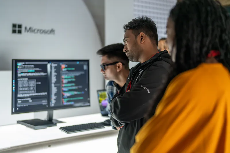 Three attendees at a workstation under the Microsoft sign.