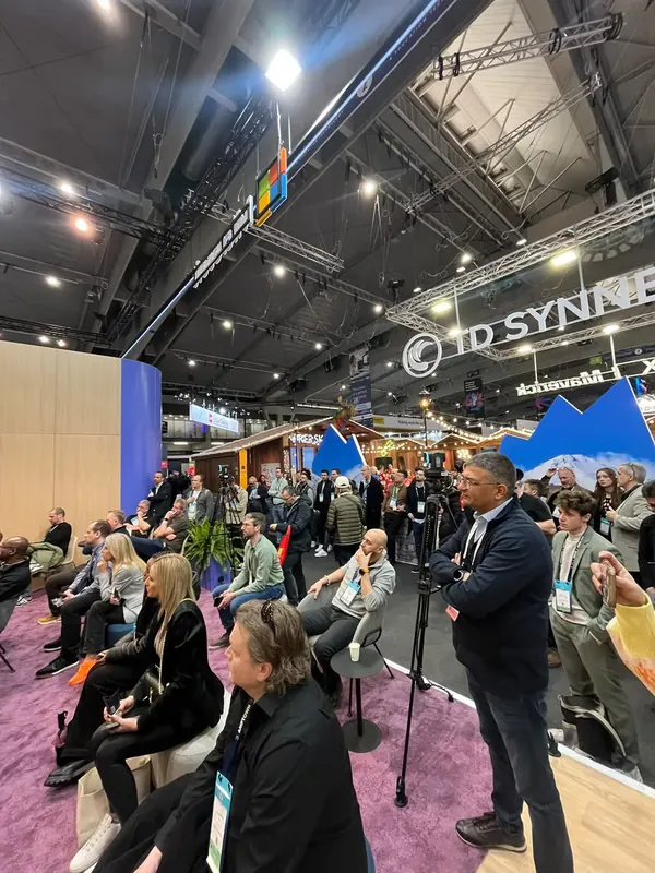 Attendees seated for a theatre session, the show floor and exhibitor rigging stretching away behind them.