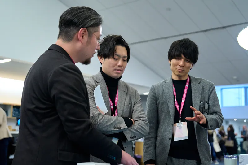 Three attendees in conversation between sessions, lanyards on.